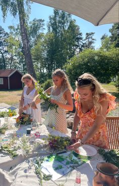 three women are standing around a table with flowers