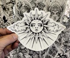 a hand holding up a sticker with an image of the sun