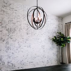 a chandelier hanging from the ceiling in front of a white brick wall with a potted plant