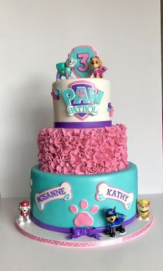 a three tiered cake decorated with paw patrol characters and pink ruffled frosting