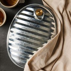 an oval serving tray with silver stripes on it next to coffee cups and saucers