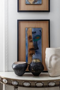 two vases sitting on top of a white table next to framed pictures and paintings