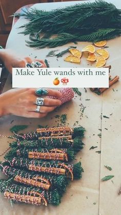 a table topped with lots of green plants and oranges next to a sign that says make yule wands with me