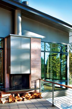 a fire place in front of a building with glass walls and wood logs on the ground