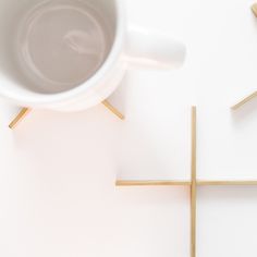 three wooden sticks sticking out of the ground next to a coffee mug and cross on a white surface