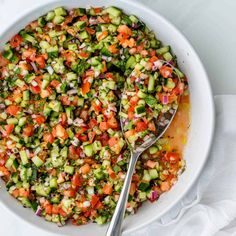 a white bowl filled with cucumber and red onion salad next to a spoon