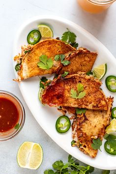 some food is on a white plate with limes and cilantro sauce next to it