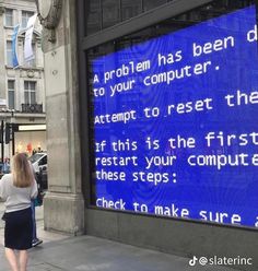 a woman walking down the street in front of a large screen with words on it