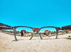 two people wearing hats and sunglasses on the beach with palm trees reflected in their glasses