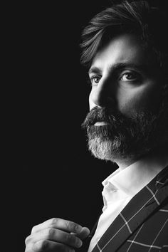 a black and white photo of a man with a beard wearing a suit, looking off to the side