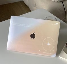 an apple laptop computer sitting on top of a white table next to a glass cup