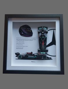 a framed photograph of a race car with the driver's helmet on display in front of it