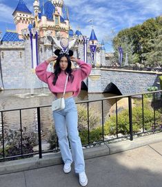 a woman standing in front of a castle with her hands on her head and wearing mickey ears