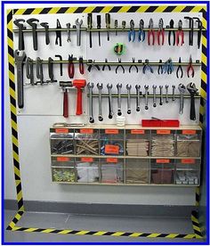 tools are hanging on the wall with yellow and black stripes around it, along with other tools in bins