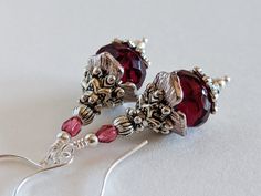 a pair of earrings with red glass beads and silver accents on white table top next to earwires