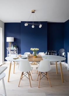 a dining room with blue walls and white chairs around the table in front of it