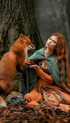 a woman with red hair sitting next to a dog in the woods near a tree