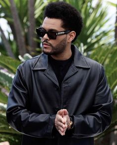 a man in black jacket and sunglasses holding his hands together