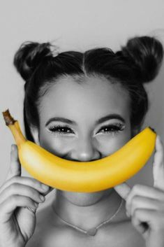 a woman holding a banana up to her face with the word smile on it's cheek