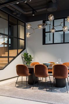 a dining room table with chairs and lights hanging from it's ceiling, next to a staircase