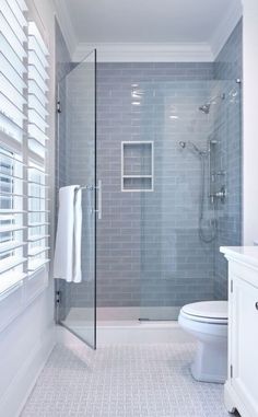 a bathroom with a walk in shower next to a white toilet and sink under a window