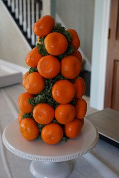 a stack of oranges sitting on top of a white cake plate in front of a staircase