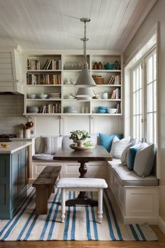 a kitchen with white cabinets, blue and white striped rugs and a bench in front of the window