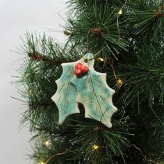 a ceramic christmas ornament hanging on a tree branch with red berries and green leaves