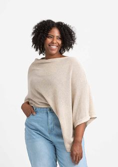 a woman wearing a beige sweater and blue jeans, standing in front of a white background