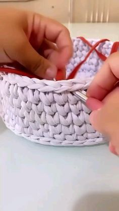 two hands crochet together in a white woven basket with red ribbon on the edge