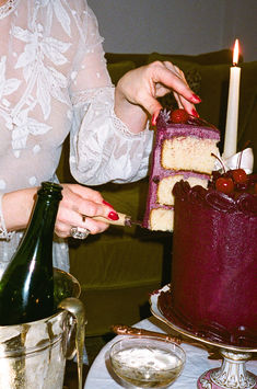 a woman is decorating a cake with cherries on it while holding a wine bottle