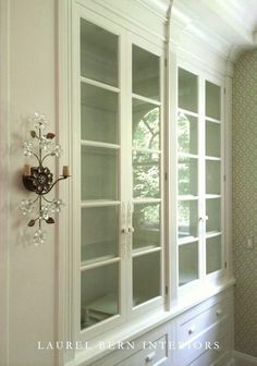 a white china cabinet with glass doors in a room that has wallpaper on the walls