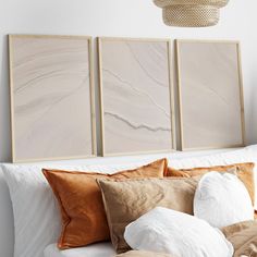 three paintings hanging on the wall above a bed with white pillows and brown throw pillows