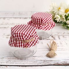 two jars with red and white gingham cloth on them sitting next to some daisies