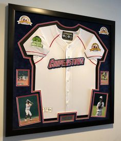 a baseball jersey is displayed in a black framed frame with photos and other memorabilia on the wall