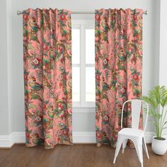 a white chair sitting in front of a window covered in pink curtain panels and flowers