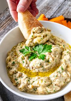 a hand dipping a piece of bread into a bowl filled with hummus and parsley