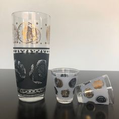 two shot glasses sitting next to each other on top of a black table with gold trimmings