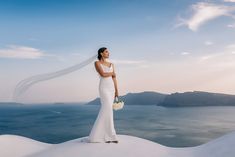 a woman in a wedding dress standing on top of a snow covered hill next to the ocean