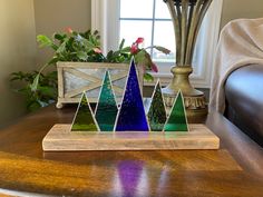 a wooden table topped with three different colored glass trees on top of it next to a potted plant