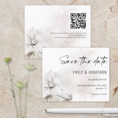 save the date cards with white flowers on them and a pen next to each other