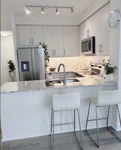 two white chairs sitting in front of a kitchen counter with a clock on the wall