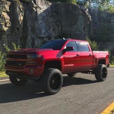 a red truck is parked on the side of the road near some rocks and grass