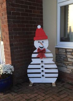 a wooden snowman with a red hat and bow tie standing in front of a brick building