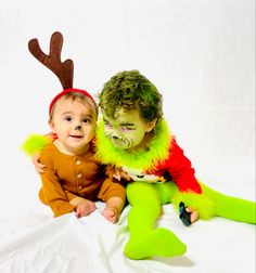 two children dressed up in costumes sitting next to each other on a white sheeted surface