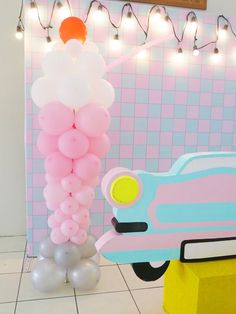 there is a pink car and balloons on the floor in front of a wall with lights