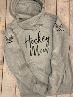 a grey hoodie with the words hockey mom printed on it sitting on a wooden floor