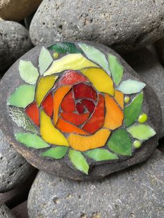 a rock with a stained glass flower on it sitting next to some rocks and leaves