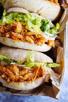 three pulled pork sandwiches with lettuce and tomato sauce in a brown paper container