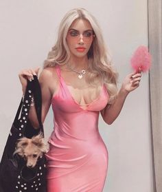 a woman in a pink dress is holding a black bag and posing for the camera